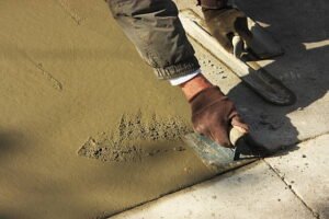 A man shovels cement onto a sidewalk as part of a concrete driveway repair project.