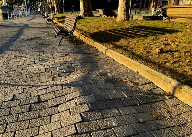 A park bench positioned on a sidewalk with an uneven surface nearby.