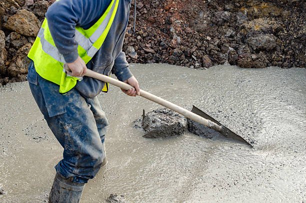 A man shovels cement onto an uneven walkway, focusing on his task in a construction setting.