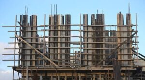 A large building under construction, featuring wooden poles and a visible load-bearing wall.