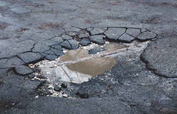 A damaged road featuring a pothole and a broken piece of wood, highlighting the need for repair work.
