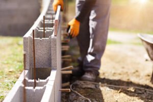 A man constructs a concrete block wall, mixing cement and placing blocks with precision on a construction site.